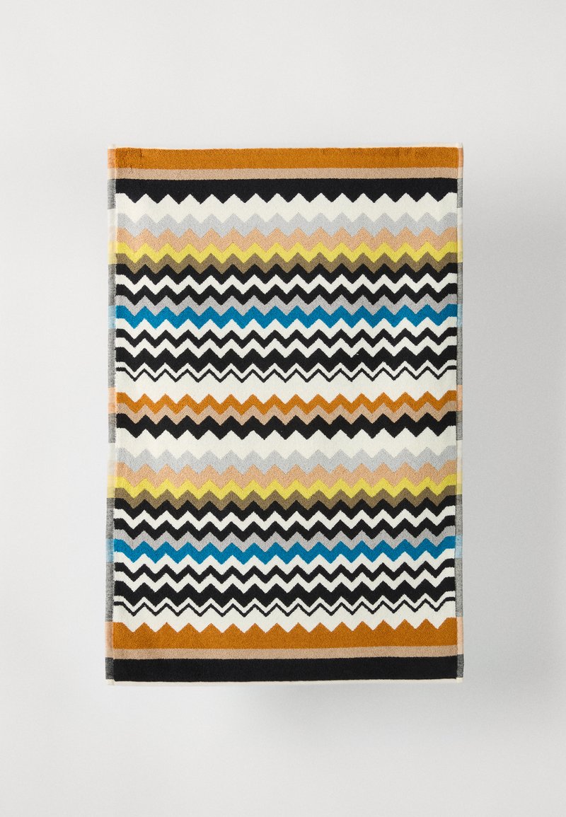 Asciugamano con motivo a zigzag multicolore, caratterizzato da righe vivaci arancioni, nere, blu e gialle, realizzato in materiale tessile morbido.