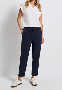 Navy jogger pants with an elastic waistband and drawstring. Paired with a white short-sleeve V-neck top and casual sneakers.