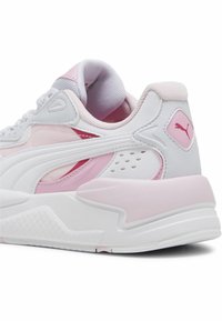 Sneakers PUMA z białą cholewką i różowymi akcentami, siateczkowymi panelami oraz teksturowaną podeszwą. Charakterystyczny detal z logo na pięcie.