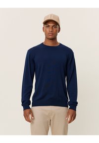 Marinblauer Strickpullover mit Rundhalsausschnitt und langen Ärmeln. Der Stoff wirkt weich und es gibt ein dezentes Logo auf der Brust.