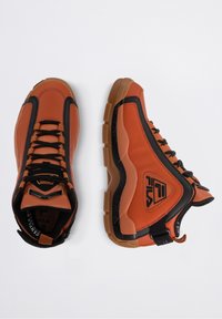 Baskets montantes orange et noires FILA avec semelles épaisses marron, laçage devant et logo sur le côté, vues de dessus et de côté sur fond blanc.
