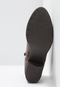 Semelle d'une botte marron à la cheville avec une semelle texturée et un petit talon, indiquant la pointure 37 en dessous.