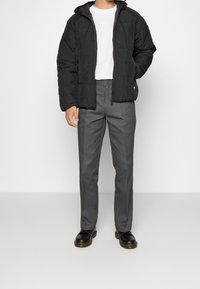 Veste matelassée noire avec capuche, t-shirt blanc, pantalon gris sur mesure et bottes noires à lacets. Design simple et moderne avec une silhouette épurée.