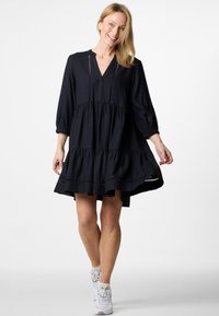 Schwarzes, schichtetes Kleid mit V-Ausschnitt, Dreiviertelärmeln und Aussparung. Aus strukturiertem Stoff gefertigt, reicht es bis über die Knie.