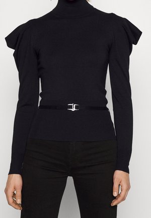 Pull noir ajusté à col roulé avec épaules bouffantes et une fine ceinture noire avec boucle argentée à la taille, porté avec un pantalon noir.