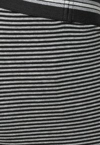 Svartvitt randigt tyg med horisontella linjer, har en mjuk textur och ett mörkt elastiskt midjeband upptill.