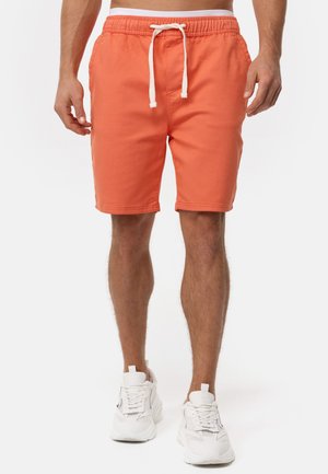 Orange shorts med elastisk talje, hvid snor, sidelommer og en afslappet pasform, parret med hvide sportssko.