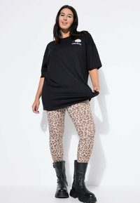 Camiseta negra de gran tamaño con logo, mallas beige con estampado de leopardo marrón, botas negras hasta el tobillo con suelas gruesas. Un atuendo simple y casual.
