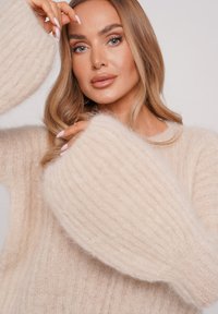 Beige, ribbed knit sweater made from soft, fluffy material. Features oversized, textured sleeves and a rounded neckline.