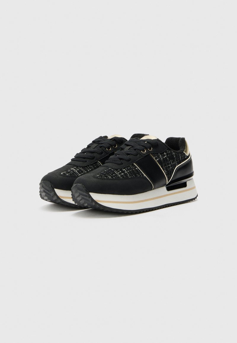 Chaussures de sport noires avec un tissu texturé, des accents dorés et une semelle intermédiaire blanche. Elles présentent un bout rond et une semelle extérieure en caoutchouc durable.