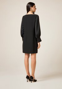 Czarna sukienka z długimi, bufianymi rękawami, gładką fakturą i kwadratowym dekoltem. Dobra do niej czarne, błyszczące szpilki. Prosty, elegancki fason.