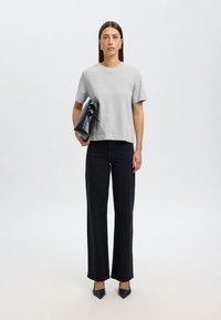 Camiseta gris de manga corta, jeans negros de pierna ancha, tacones negros de punta y un bolso negro estructurado sujeto con un brazo, diseño sencillo y moderno.
