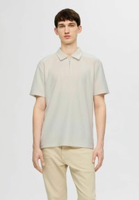 Polo tričko s krátkým rukávem v světle šedé barvě, vyrobené z texturované látky s límcem na zip, s volným střihem a minimalistickým designem.