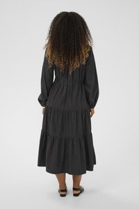 Juoda maksi suknelė su ilgomis rankovėmis, prigludusia liemens dalimi ir laisvais sijonais. Audinys turi subtilų raštą. Pabrėžta elastinga juosmens dalimi.