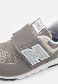 Chaussure de sport en maille et daim gris avec une sangle Velcro. Dotée d'un grand logo 'N' blanc et d'un col rembourré. Semelle en caoutchouc avec des accents noirs.