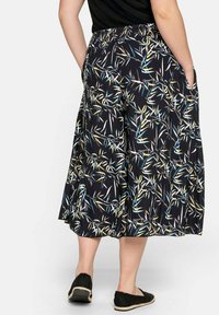 Květinový vzor na kalhotách culottes z černé látky, s nařaseným pasem a bočními kapsami. Akcenty modré a žluté na tmavém pozadí.