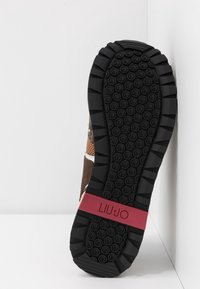 Sohle eines Turnschuhs mit schwarzem Profil, das kreisförmige Griffe aufweist, und einem roten Band in der Mitte mit dem eingravierten "LIU·JO"-Logo.