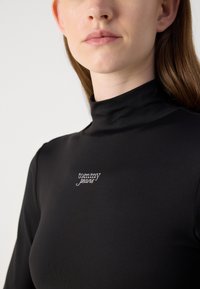 Svart rullekrage-genser laget av glatt stoff med en liten hvit brodert "tommy jeans"-logo på brystet. Tettsittende design.
