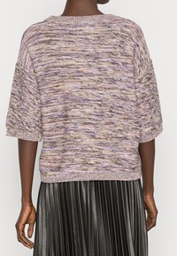 Pull en maille dans des teintes mauve, lavande et beige. Coupe oversize avec des manches courtes et un ourlet côtelé. Fil texturé avec une légère variation de motif.