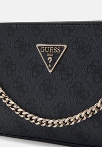 Czarna torebka o teksturowanej powierzchni z złotym łańcuszkowym paskiem i trójkątną blaszką z logo z wytłaczanym wzorem oraz złotymi akcentami.
