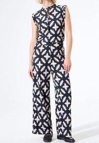 Granatowy kombinezon w geometryczne kremowe wzory, z krótkimi falbankowymi rękawami, okrągłym dekoltem i szerokimi spodniami.