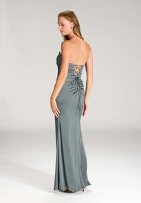 GRAUES SATIN ABENDKLEID MIT ENGANPASSENDEM SILHOUETTE, RÜSCHENDETAILLING UND EINEM SCHNÜRRICKEN-DESIGN. BODENLANGE AUSFÜHRUNG MIT EINER GLATTEN TEXTUR.