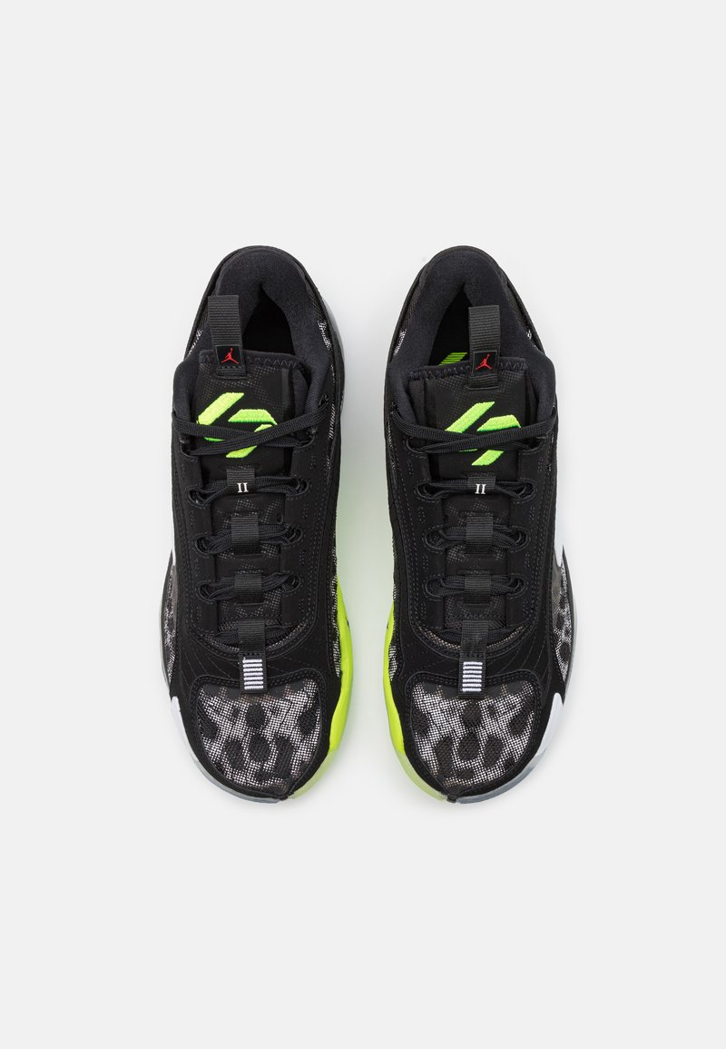 Zapatos deportivos negros con acentos en verde neón, tela texturizada y suela con patrón. Cuentan con un diseño de cordones y una marca en la lengüeta.