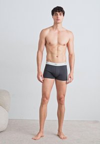 Dunkelgraue Boxershorts mit einem weißen Bund, körperbetontes Design, glatte Textur und ohne sichtbare Muster, getragen von einem männlichen Model vor einem hellen Hintergrund.