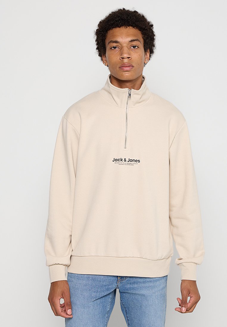 Sudadera de forro polar beige con cuello alto, cremallera de medio frente y logotipo frontal en negro. Presenta puños de canalé y un corte relajado.