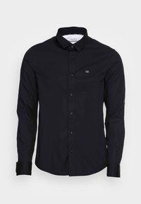 Camicia nera a maniche lunghe in cotone, con colletto button-down, bottoni frontali e piccolo logo CK bianco sul petto.