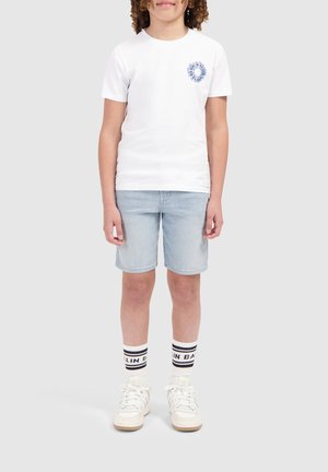 Witte T-shirt met korte mouwen met een blauwe grafische afbeelding op de borst, gecombineerd met lichte denimshorts en witte sneakers met zwart gestreepte sokken.