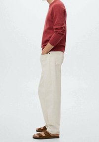 Maglione rosso a maglia, pantaloni di cotone crema e sandali in suede marrone. Il maglione ha polsini a coste e i pantaloni sono a gamba dritta con tasche laterali.