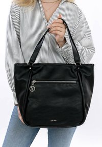 Sac cabas en cuir noir avec une surface texturée, une poche zippée argentée et un logo. Il présente des doubles poignées et un design spacieux.