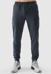 Heren sportieve broeken in donkergrijs met een elastische tailleband, taps toelopend ontwerp, een gladde textuur en zijzakken. Gedragen met grijze sneakers.