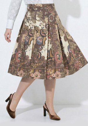 Kvinde iført en plisseret midinederdel med brunt blomsterprint og brune fløjls-højhælede slingback-sko.