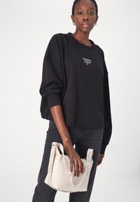 Black long-sleeve sweatshirt with "tommy jeans" logo, paired with dark jeans and a white textured handbag featuring "Calvin Klein Jeans" strap.