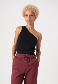Top a righe nera con design asimmetrico abbinato a pantaloni bordeaux con vita regolabile e vestibilità comoda.