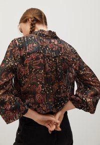 Blusa a maniche lunghe in tessuto nero trasparente con motivi floreali e fogliari colorati, con scollatura arricciata e maniche gathered.