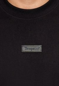 Black cotton t-shirt featuring a round neckline and a rectangular, transparent gray logo patch with "Dropsize" text. Smooth texture.