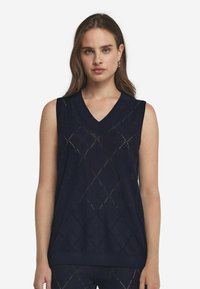 Marinblå ärmlös tröja med V-ringning, med ett diamantmönster och ribbade kanter. Tillverkad av lätt stickad material.