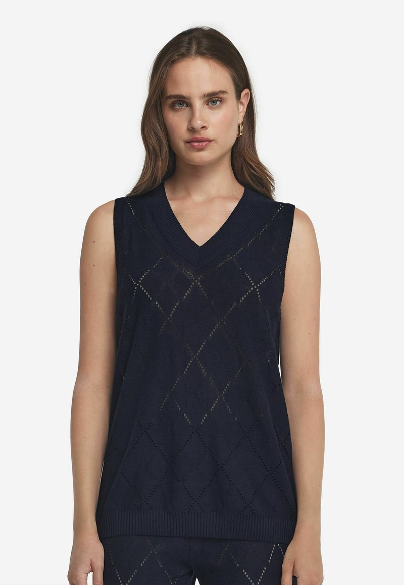 Marinblå ärmlös tröja med V-ringning, med ett diamantmönster och ribbade kanter. Tillverkad av lätt stickad material.