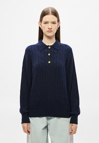 Μπλε ναυτικό πουλόβερ πλεκτό με γιακά και τρία χρυσά κουμπιά. Διαθέτει μακριά μανίκια και ριμπ μανσέτες.