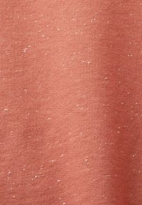 Gros plan d'un tissu corail doux et texturé avec de petites taches blanches dispersées sur toute sa surface tissée.