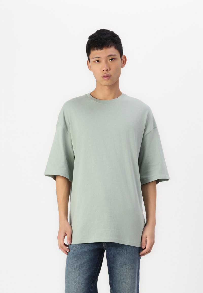 Grønn oversized t-skjorte laget av myk bomull, med korte ermer og rund halslinning, sammen med blå denimjeans.