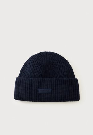 Bonnet tricoté côtelé bleu marine foncé avec bord plié et petite étiquette rectangulaire de la marque à l’avant.