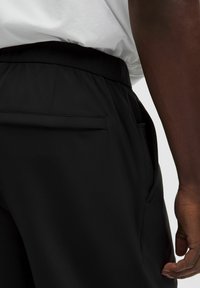 Sorte atletiske shorts med elastisk talje, sidelomme og glat tekstur. Designet er enkelt og funktionelt.