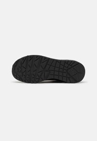 Black rubber shoe sole with a textured, patterned grip featuring angular shapes and deep grooves for traction.