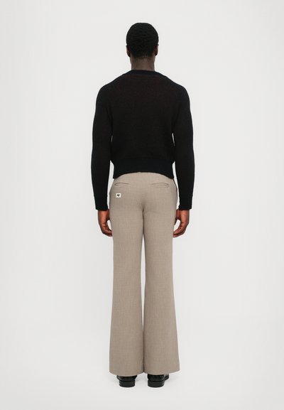 Pulover negru din tricot cu tiv cu nervuri, asortat cu pantaloni bej evazați, cu buzunare la spate și o mică etichetă cu logo.