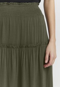 Gonna fluida verde oliva con vita smock e dettagli arricciati. Realizzata in tessuto leggero con una finitura morbida e testurizzata.