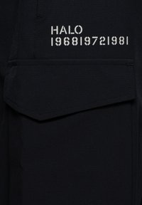 Svart tyg med en slät textur har en ficka och silvertryckt text: "HALO 196819721981" i en fet, modern stil.